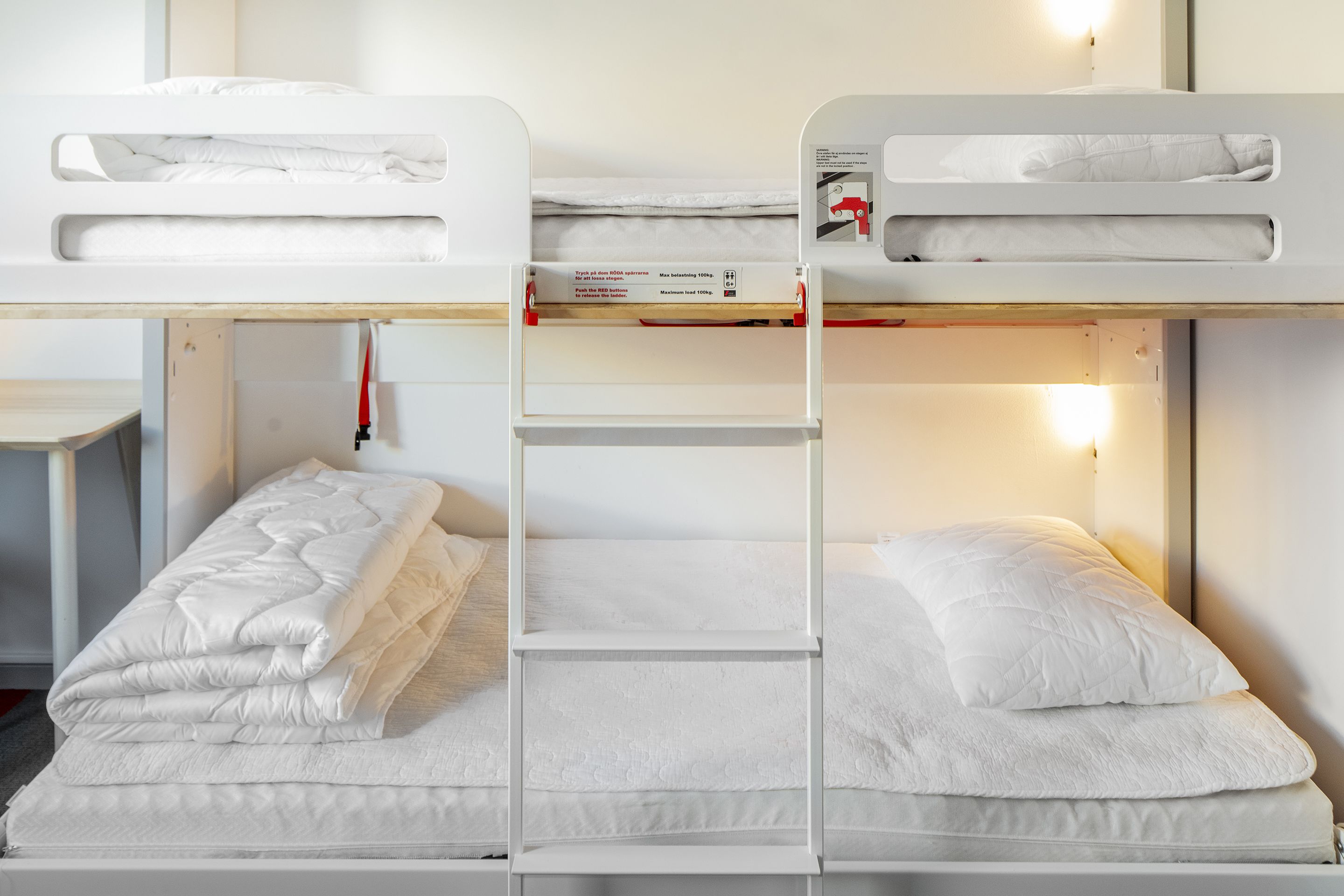 Un letto a castello con scaletta, biancheria bianca e un piccolo tavolino.