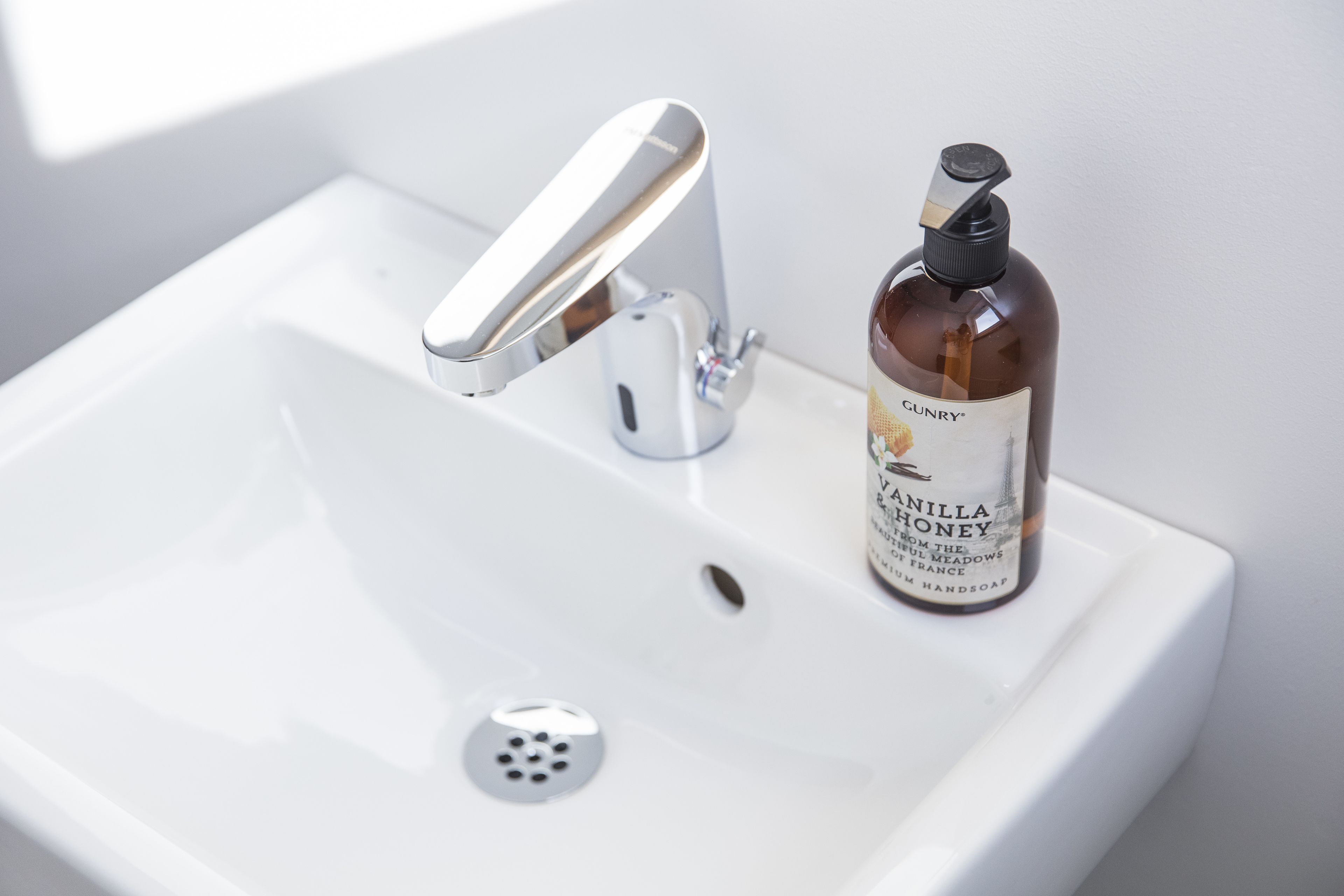 A bathroom sink with a modern faucet and a bottle of hand soap labeled "GUNRY Vanilla Honey."