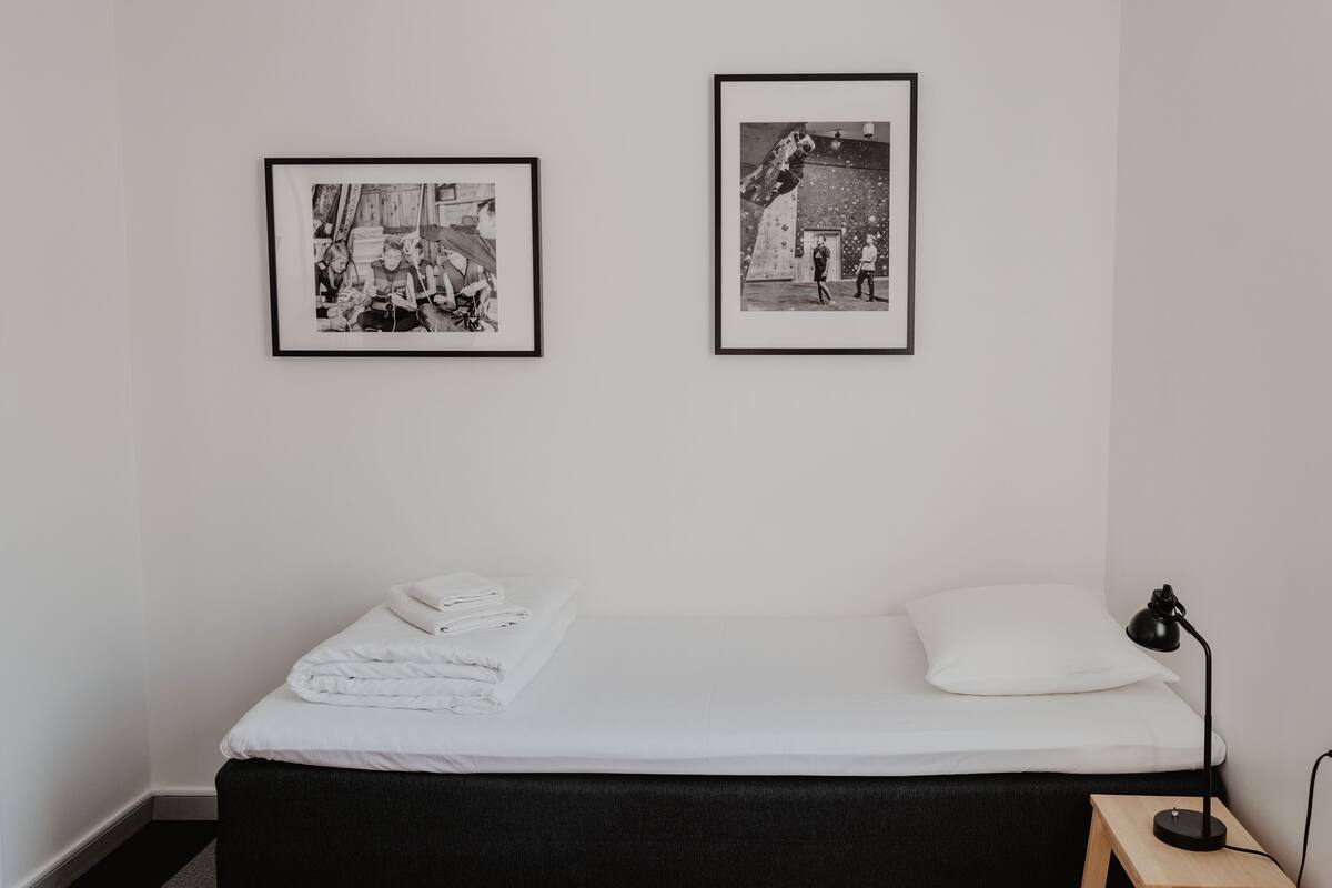 Ein Schlafzimmer mit einem Bett, einem kleinen Holzschemel und zwei gerahmten Bildern an der Wand.