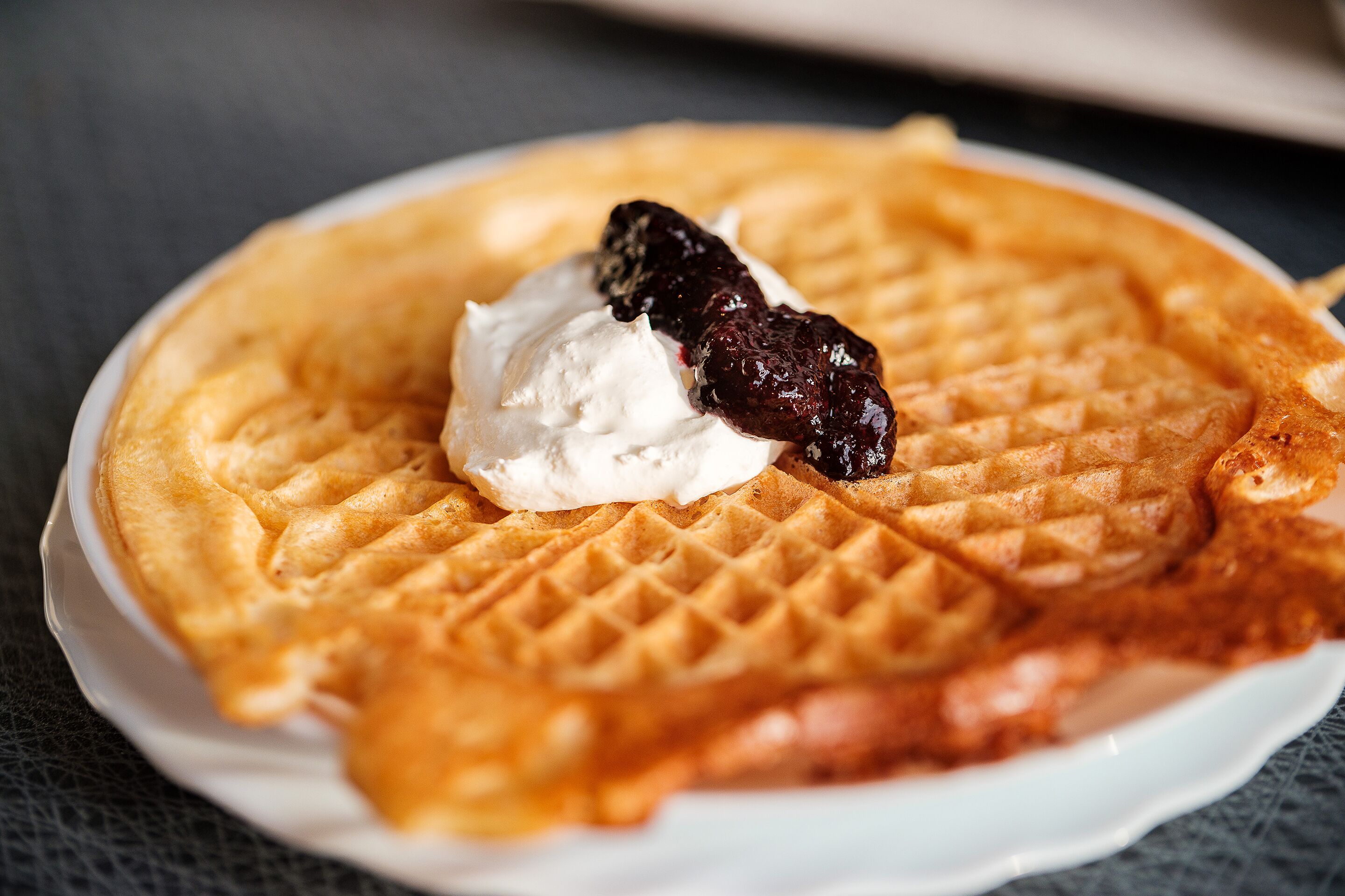 Een wafel met slagroom en een bessenfruitje op een bord.