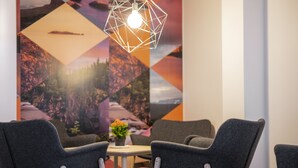Una habitación moderna con dos sillones grises, una mesita con una planta en maceta y una lámpara con diseño geométrico.