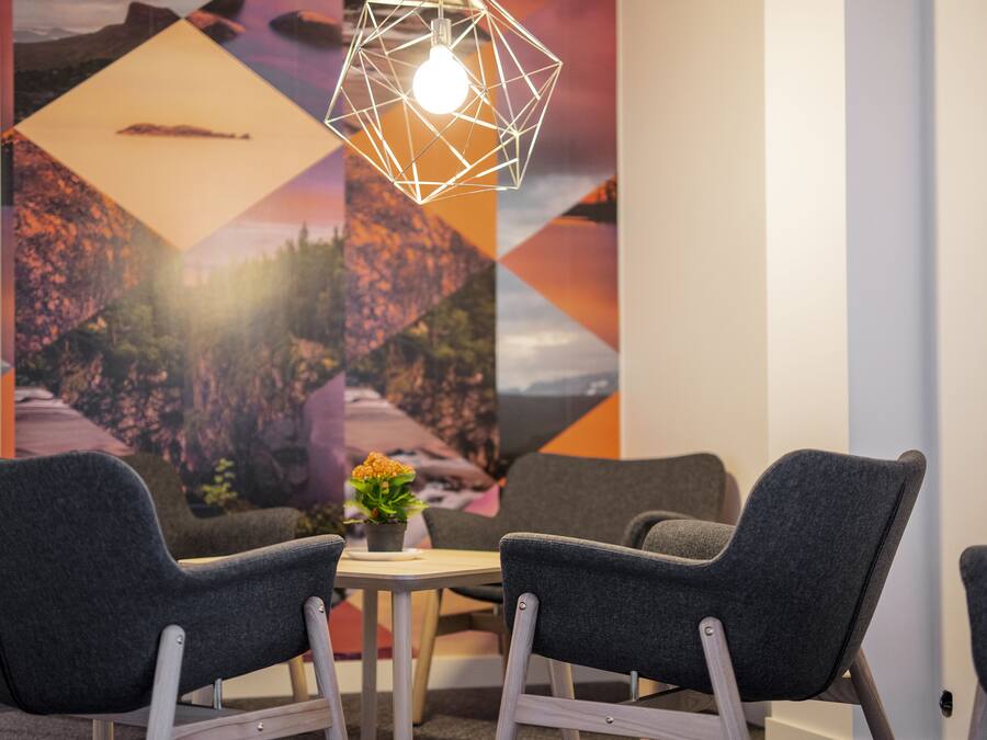 Een moderne kamer met twee grijze fauteuils, een bijzettafeltje met een bloempot en een geometrisch armatuur.