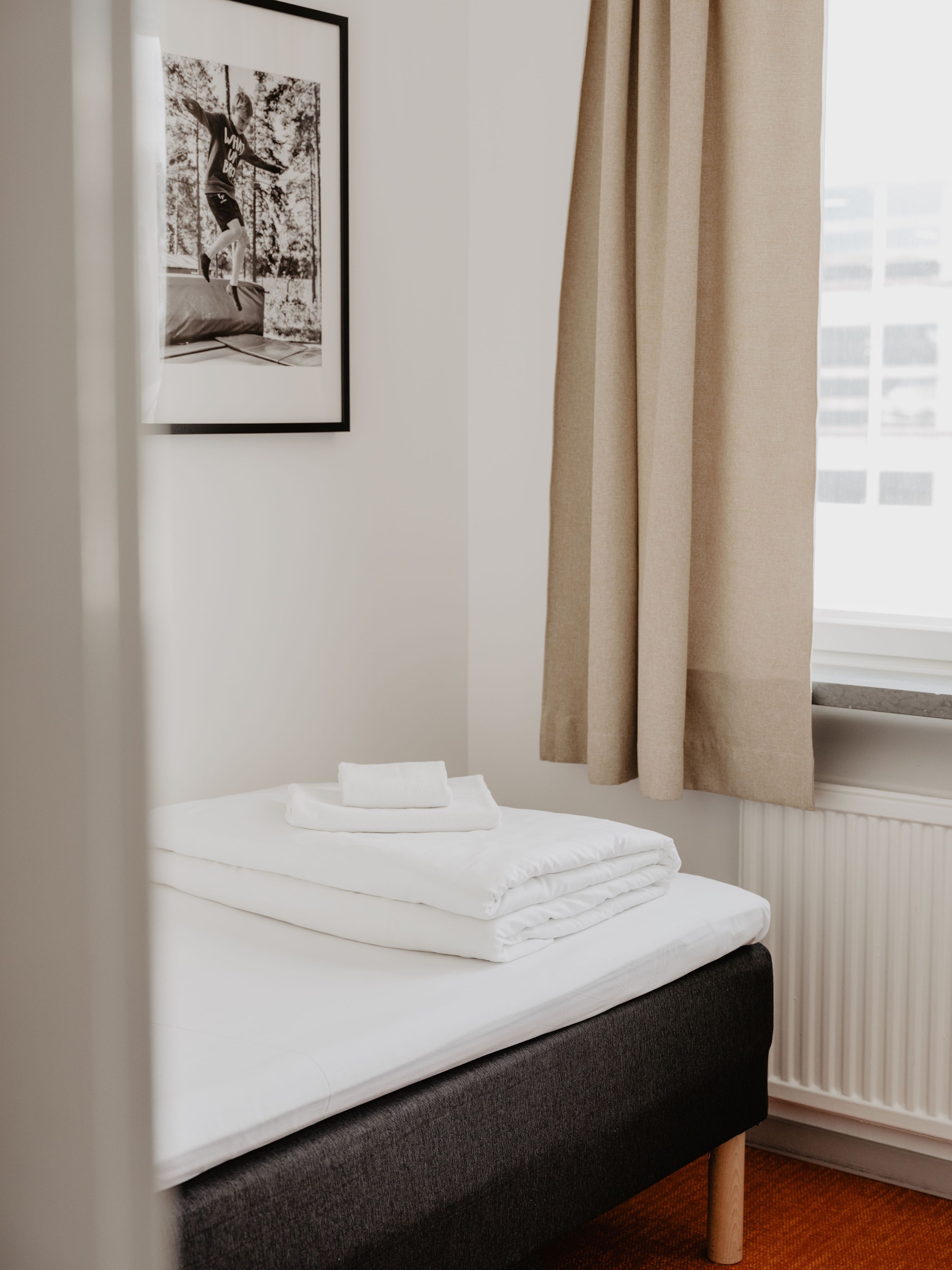 A neatly made bed with white linens, a framed photo on the wall, and a window with curtains.
