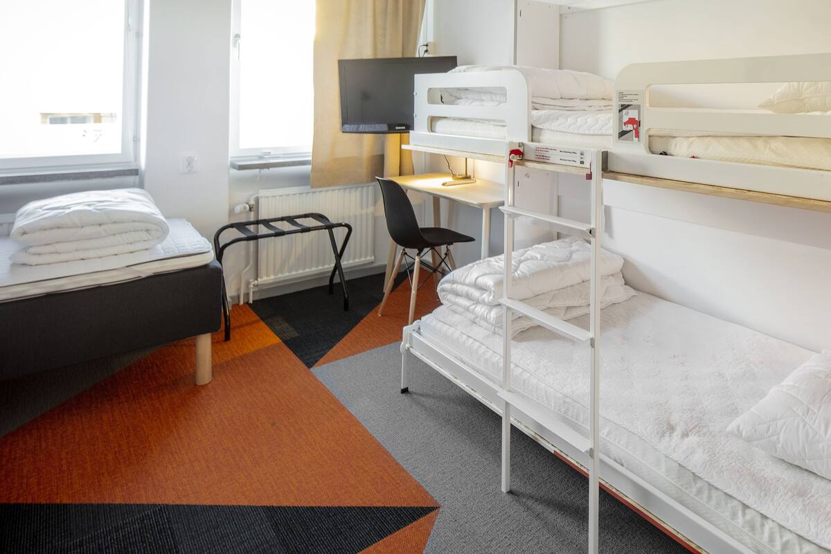 Ein Hotelzimmer mit einem Etagenbett, einem Schreibtisch mit Stuhl, einem Fernseher und einer Heizung.