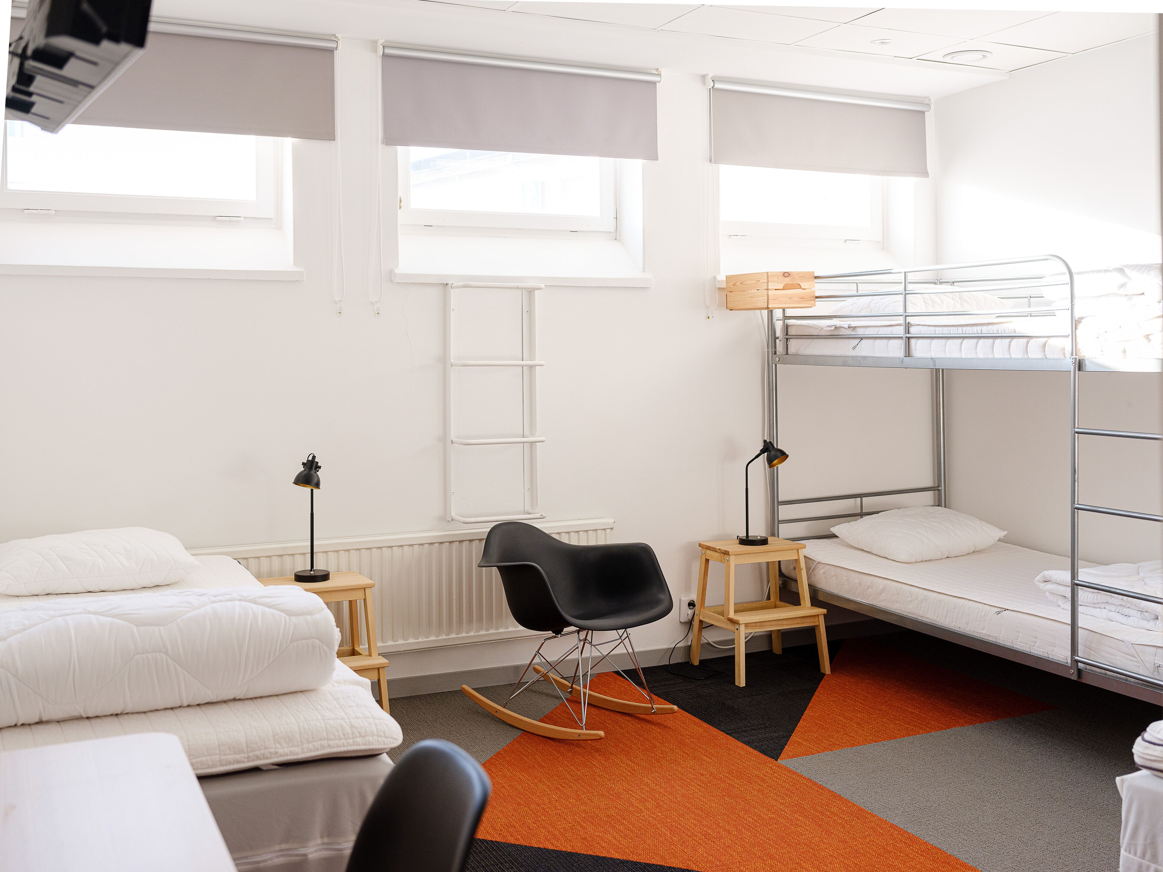 A dormitory room with bunk beds, a rocking chair, a desk, and a radiator.