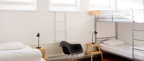 A dormitory room with bunk beds, a rocking chair, a desk, and a radiator.