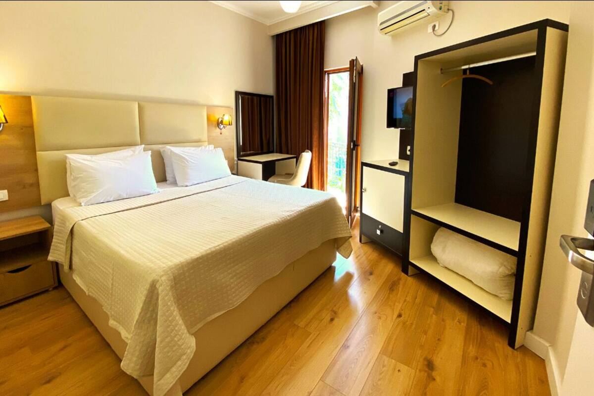 Habitación de hotel con una cama grande, mesitas de noche, televisión, armario y espejo.