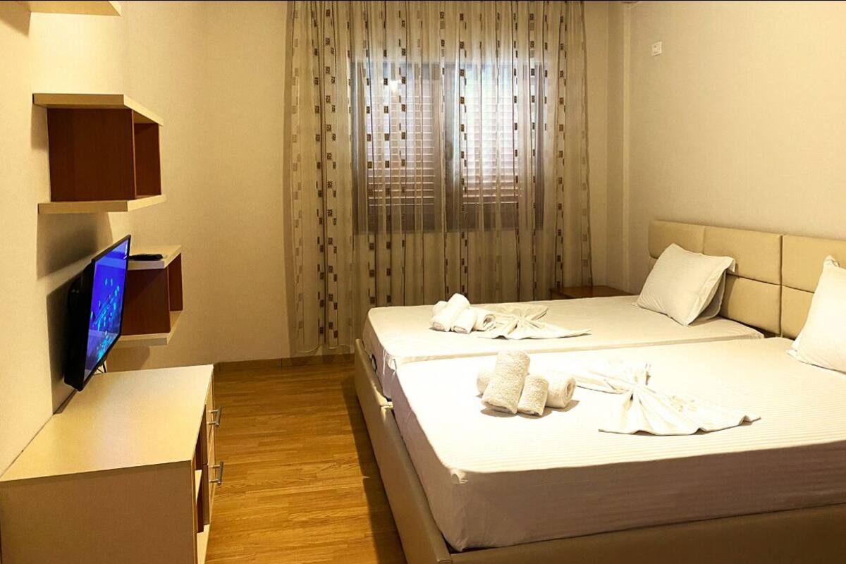 Habitación de hotel con dos camas, un televisor sobre un mueble y una ventana con cortinas.