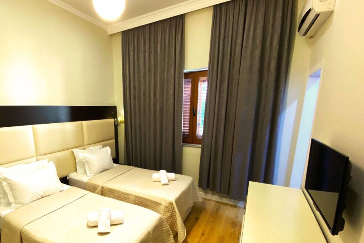 Una habitación de hotel con dos camas, televisión y ventana con cortinas.