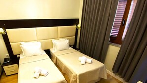 Habitación de hotel con dos camas, cada una con cubrecama y almohadas blancas, suelo de madera y una ventana con cortinas.