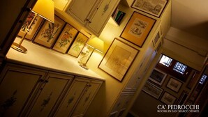 A room with framed artwork on the walls, a lamp on the counter, and a view of Venice through a window. - Ca' Pedrocchi (Venice)