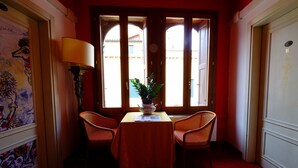 A room with a table and two chairs, a window with a view, a lamp, and a painting on the wall. - Ca' Pedrocchi (Venice)