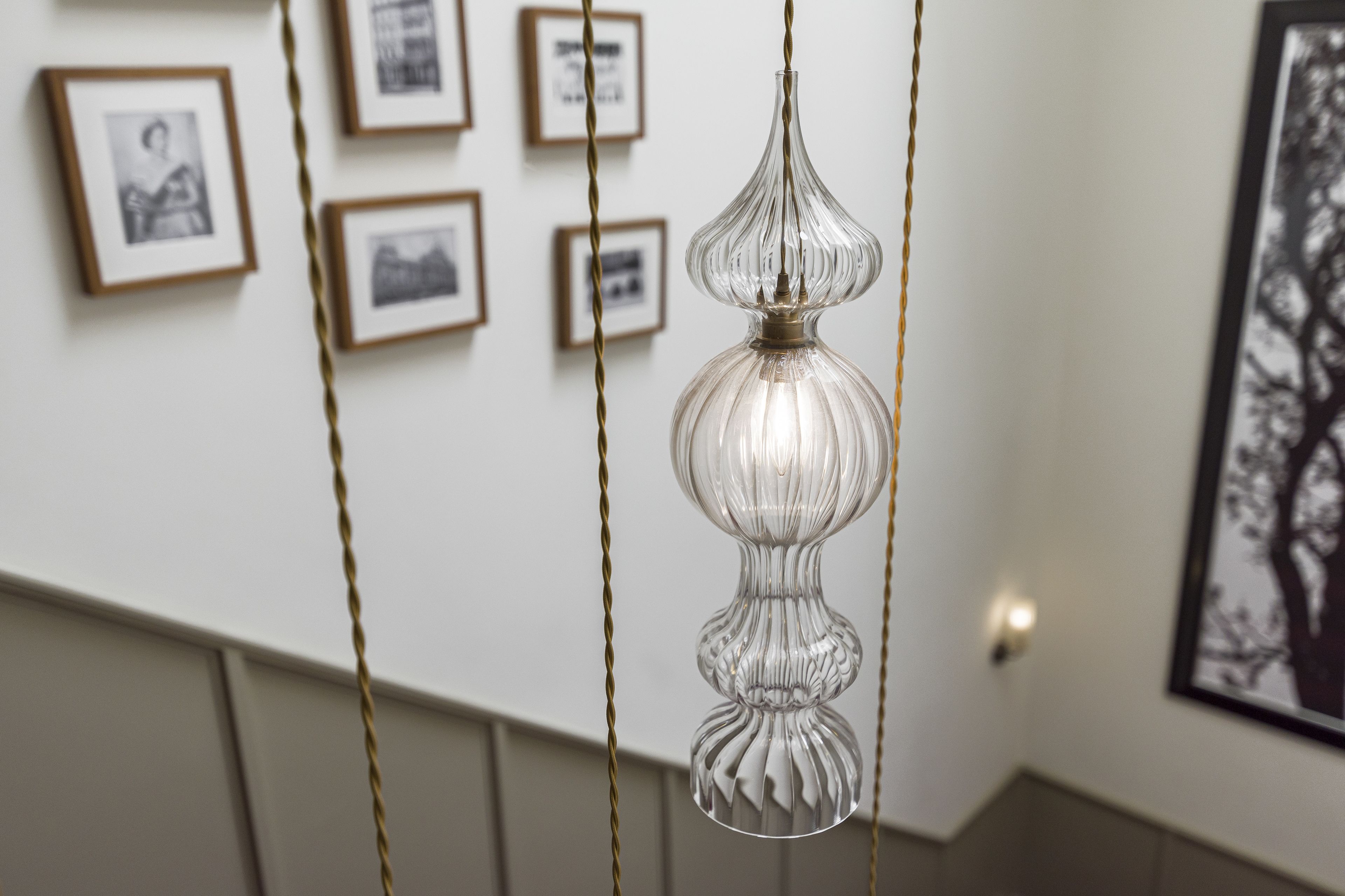 Un lustre au design original est suspendu dans une pièce dont les murs sont ornés de tableaux encadrés.