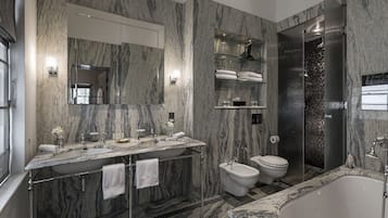 Un baño moderno con paredes de mármol, un lavamanos grande con dos espejos, un bidé, un inodoro y una bañera.