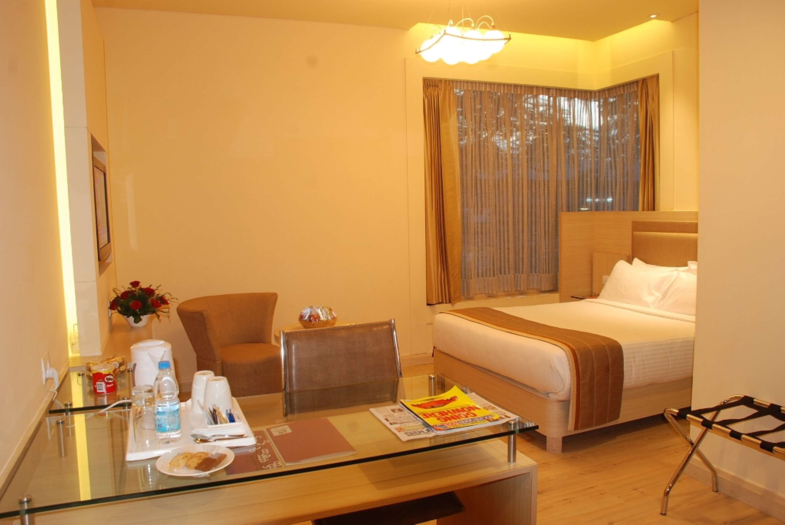 A hotel room with a bed, a glass table with amenities, a chair, and a window with curtains.