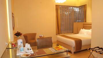 A hotel room with a bed, a glass table with amenities, a chair, and a window with curtains.