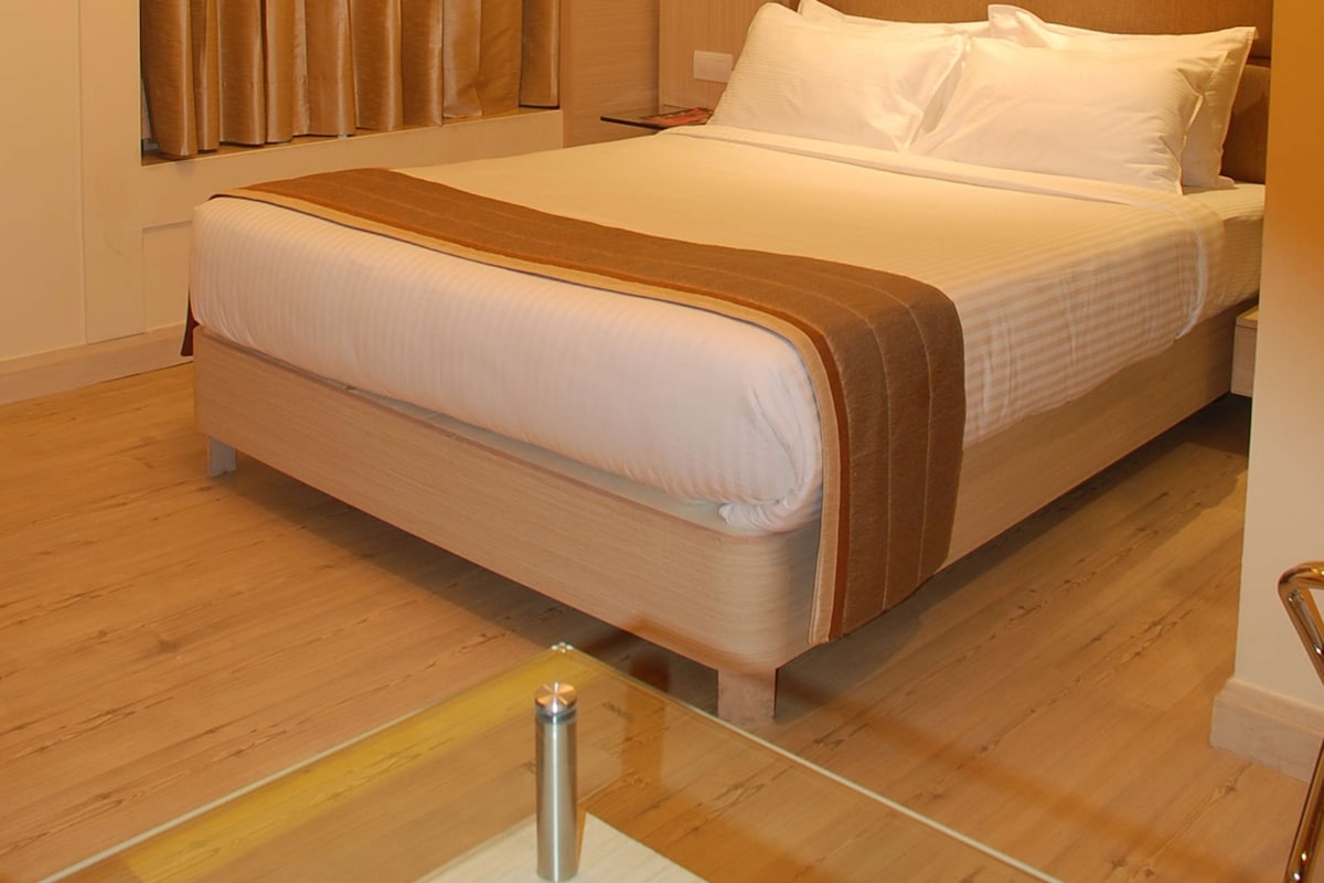 Quarto de hotel com cama, cortinas, cabeceira e mesa de cabeceira.