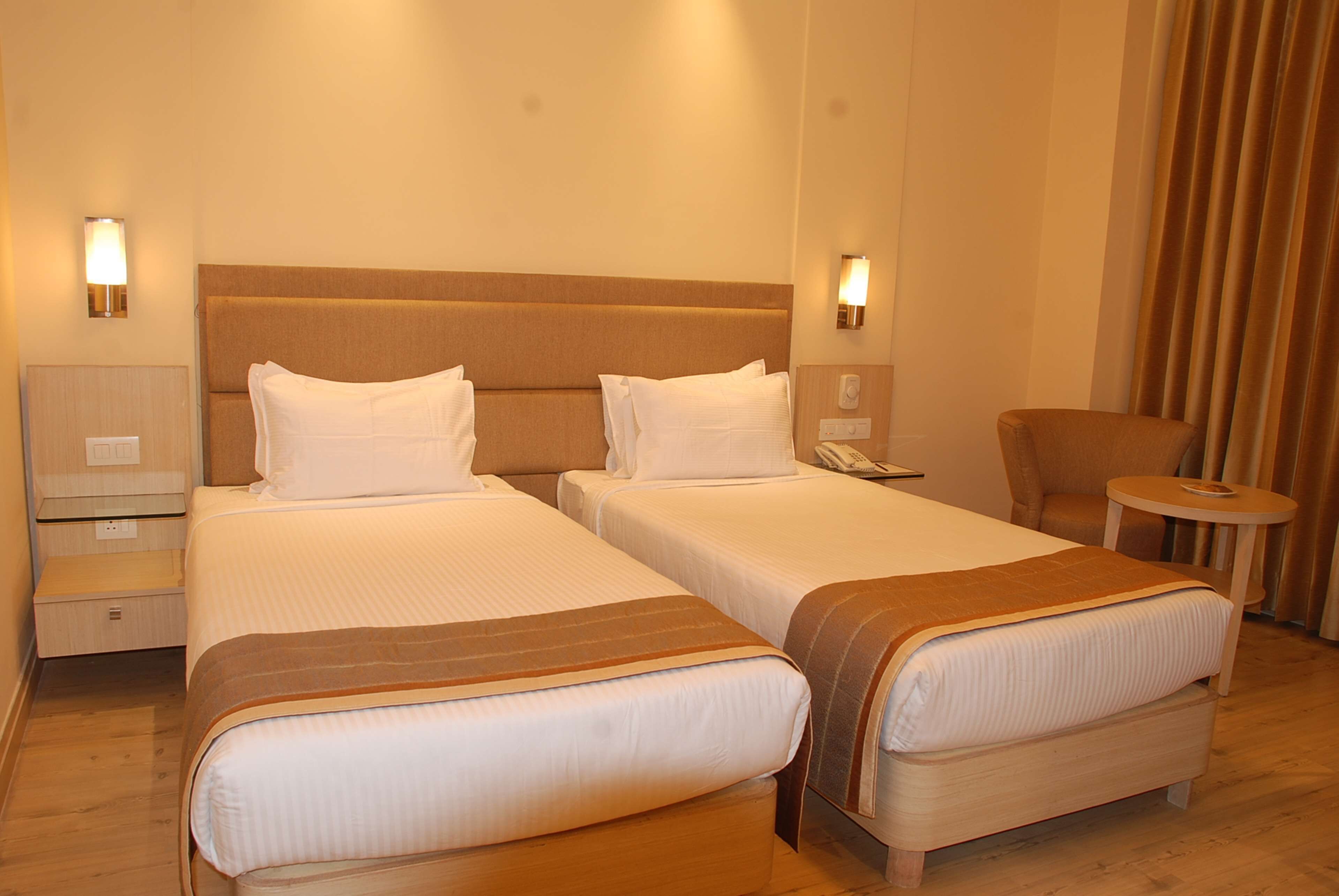 Ein Hotelzimmer mit zwei Betten, einem Sessel, einem kleinen Tisch und einer Lampe.