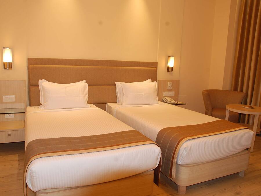 Ein Hotelzimmer mit zwei Betten, einem Sessel, einem kleinen Tisch und einer Lampe.