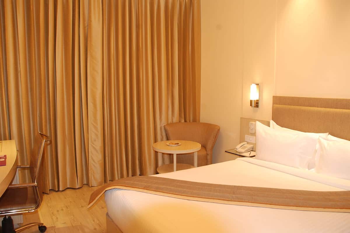 Una habitación de hotel con cama, una silla, una mesita, lámpara y teléfono.