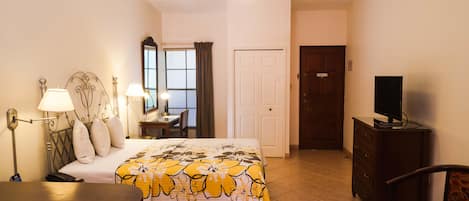 Ein Hotelzimmer mit Bett, Nachttisch, Lampe, Sessel, Fernseher, Kommode und Tür.