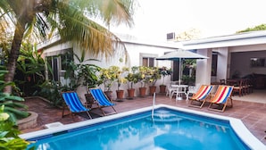 A swimming pool with blue water, surrounded by potted plants and two lounge chairs. - Hotel El Almendro (Managua)