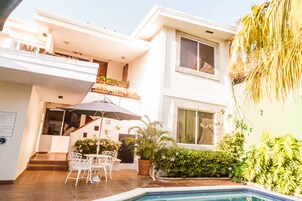 Una casa moderna de dos pisos con piscina, mobiliario exterior y abundante vegetación.