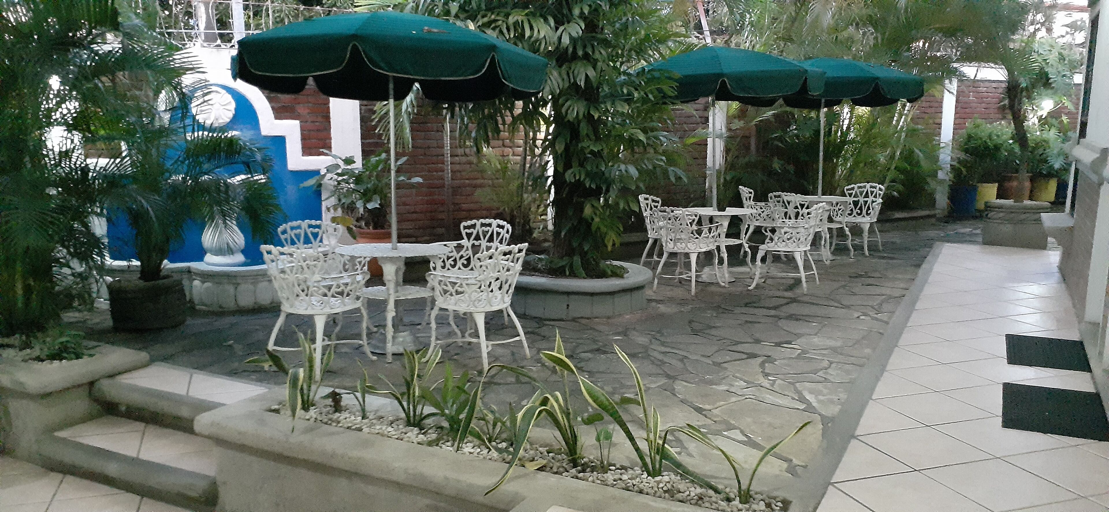 An outdoor patio with white metal chairs and tables, green umbrellas, and potted plants.