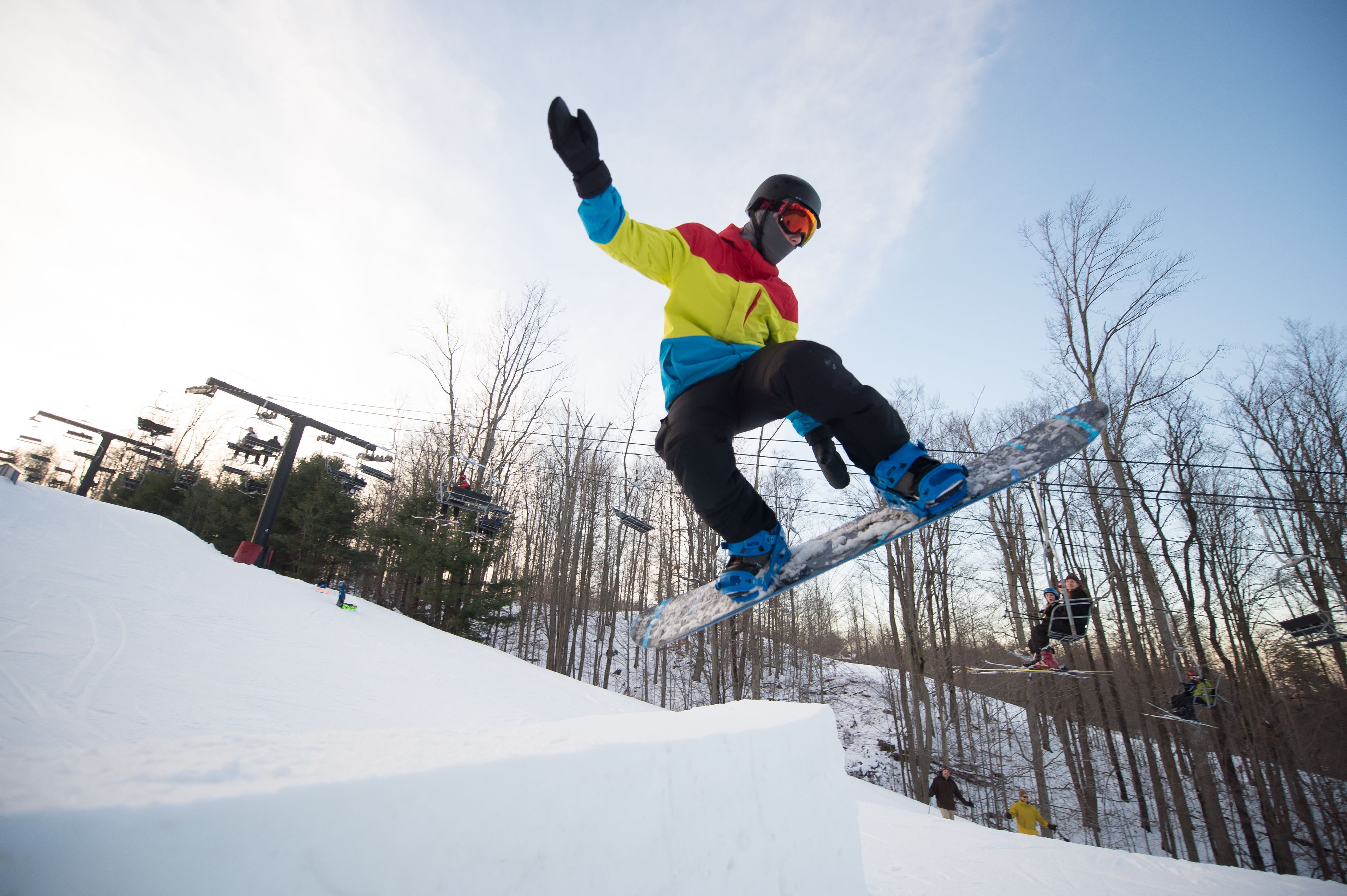 A snowboarder performing a jump on a snowy slope with trees in the background.