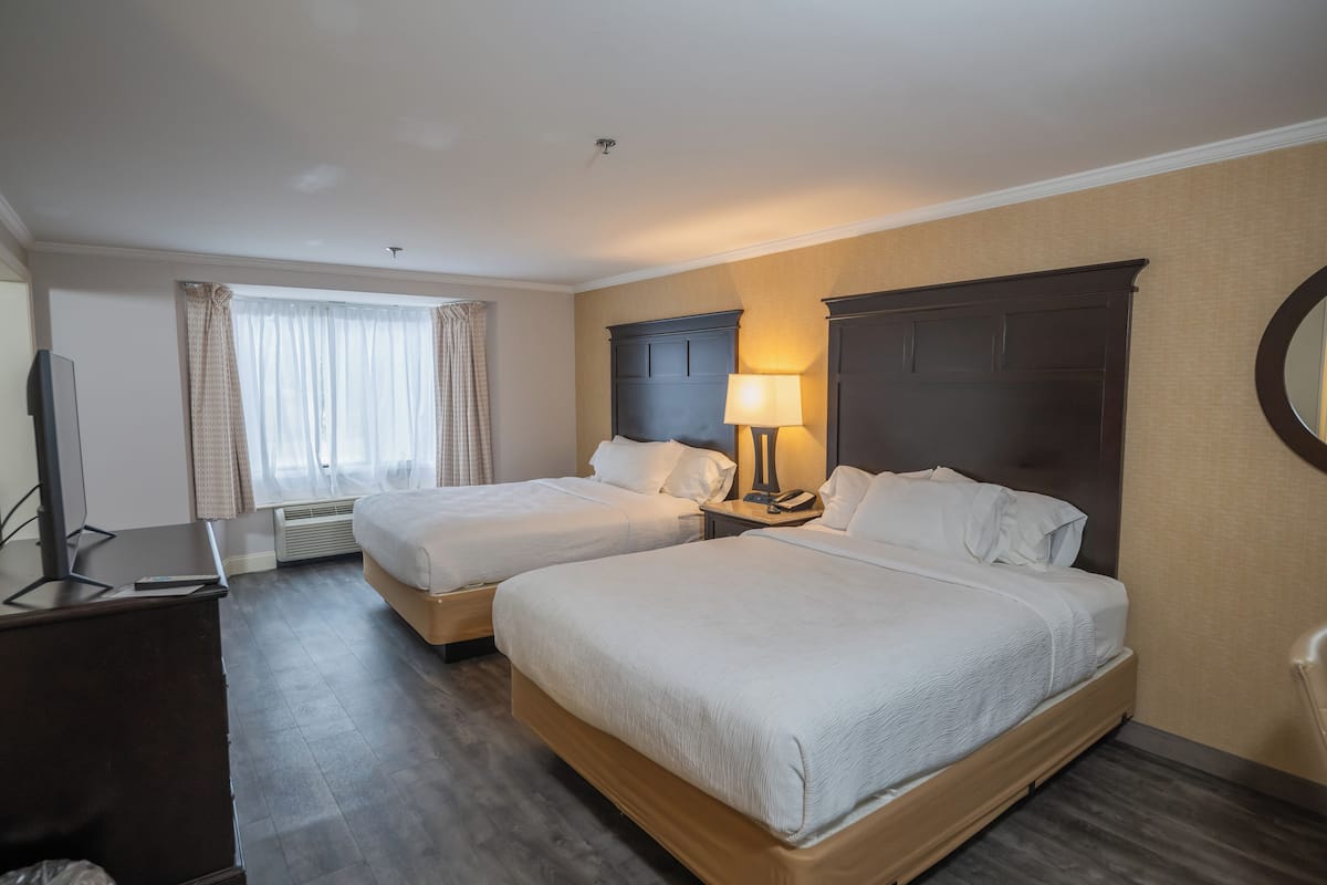 A hotel room with two beds, a desk, a TV, and a lamp.