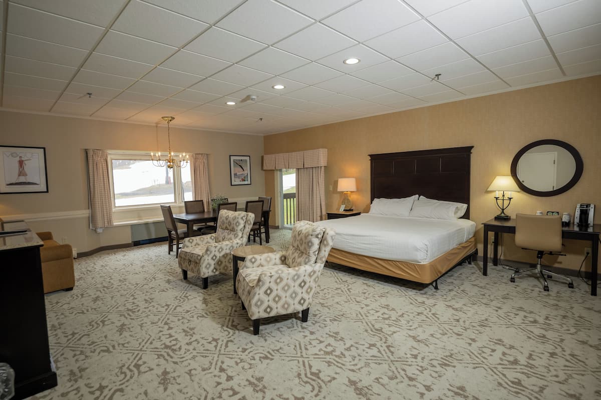 A hotel room with a large bed, two armchairs, a desk, and a computer.