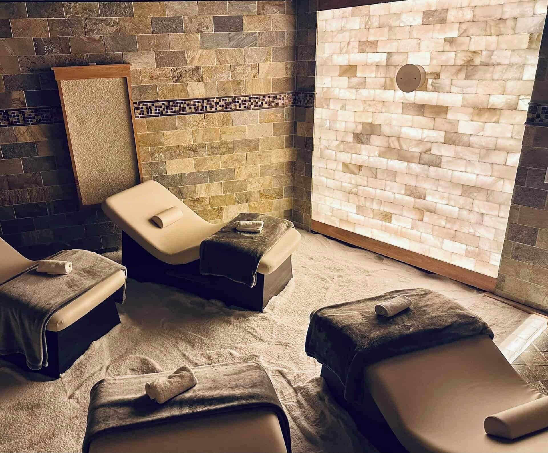 A spa room with two massage tables, a stone wall, and a large window.