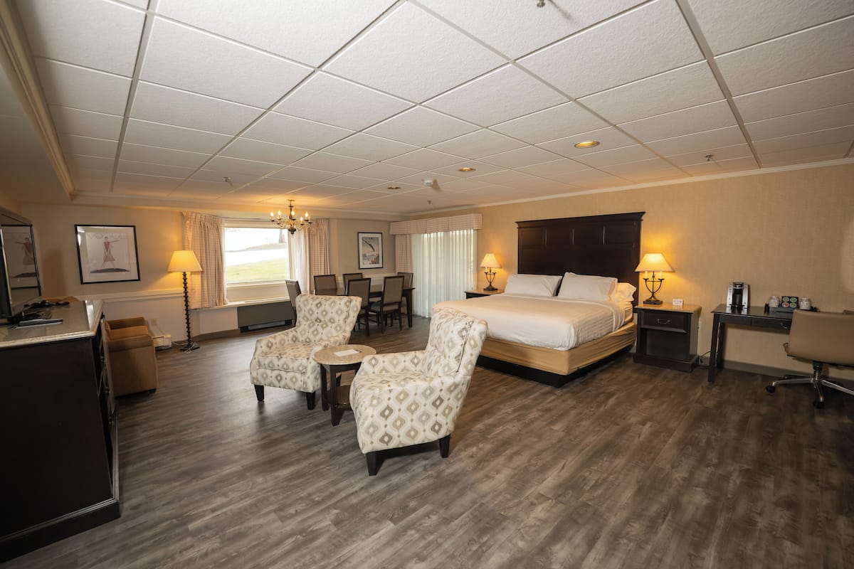 A hotel room with a large bed, two armchairs, a desk, a chair, a small table, and a window with curtains.