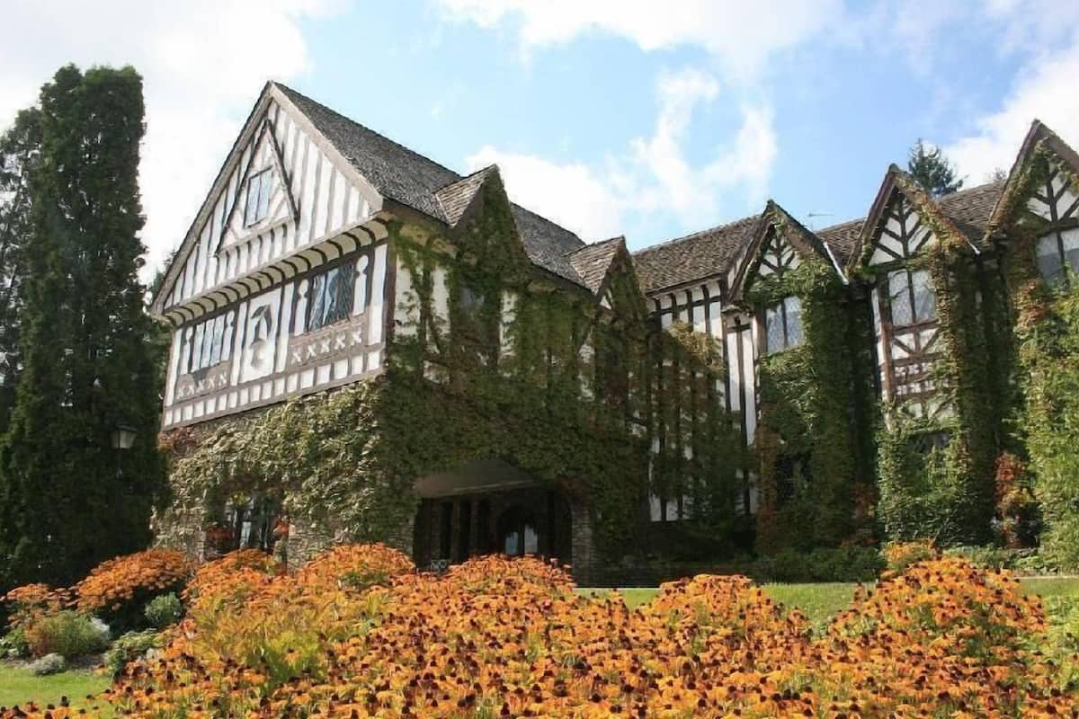 A Tudor-style building with a symmetrical facade, a central entrance with a covered porch, and a garden with orange flowers.