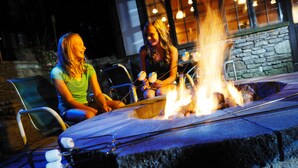 Two people sitting by a stone fire pit with a metal table and chairs. - Peek'n Peak Resort Trademark Collection by Wyndham (Clymer)