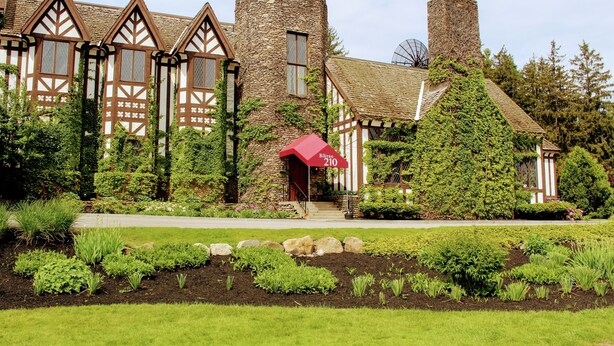 A Tudor-style building with stone walls, a red awning, and a well-maintained garden with various plants and a stone pathway. - Peek'n Peak Resort Trademark Collection by Wyndham (Clymer)