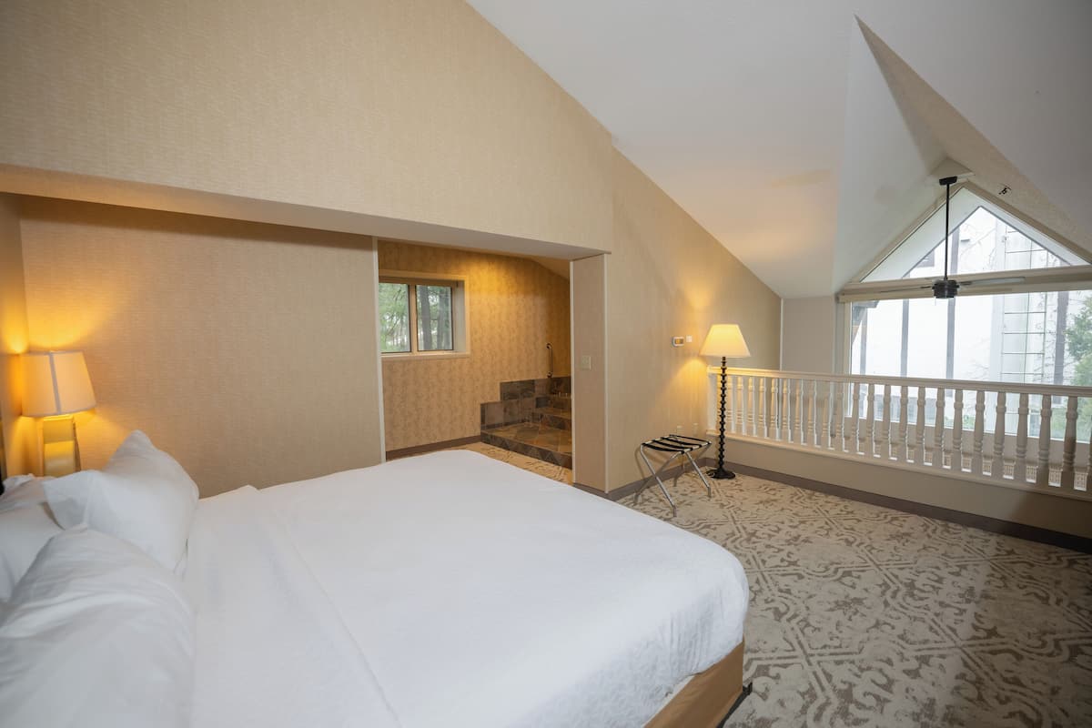 A hotel room with a large bed, a staircase leading to an upper level, and a balcony with a railing.