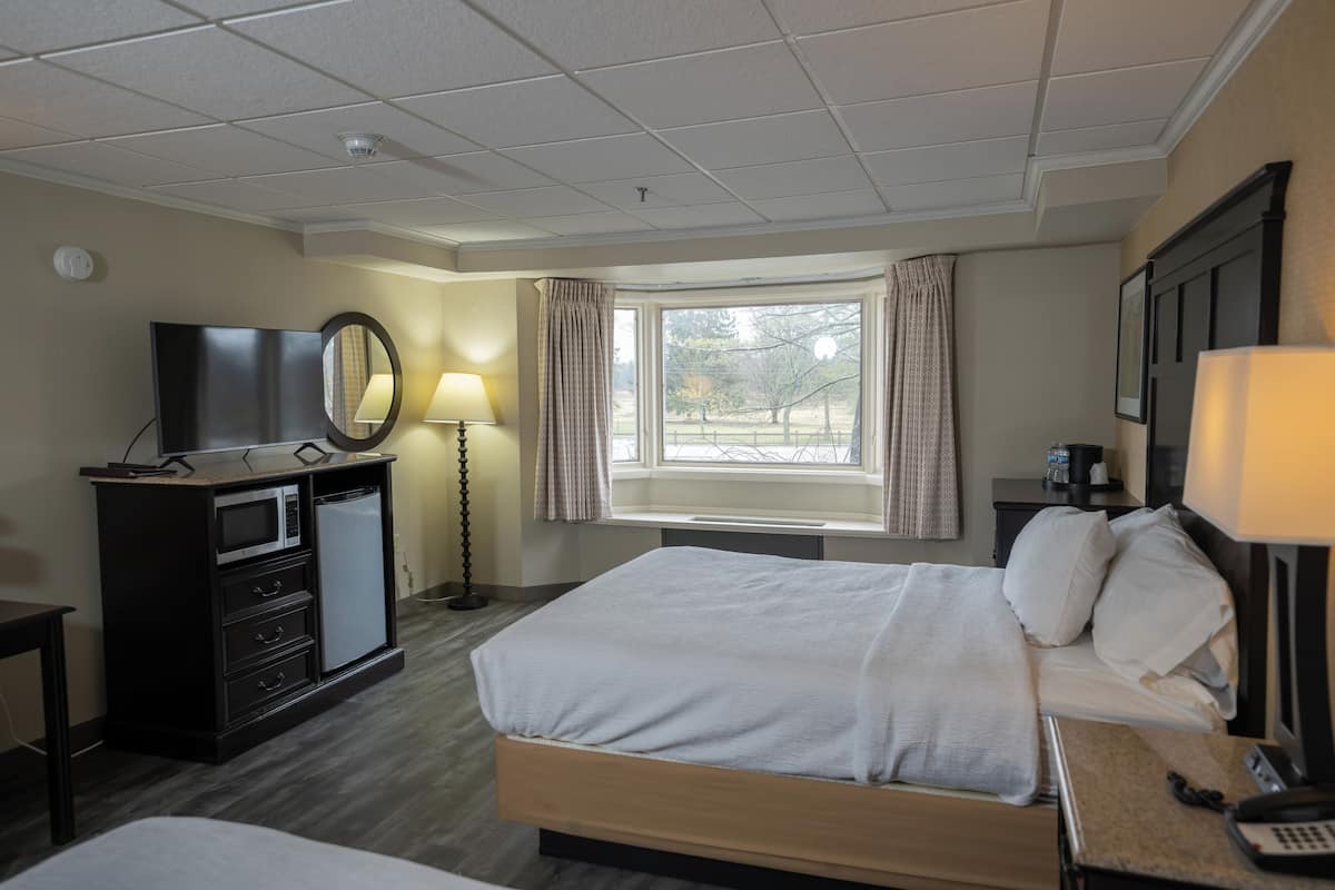 A hotel room with a bed, a desk with a computer, a TV, and a window with curtains.
