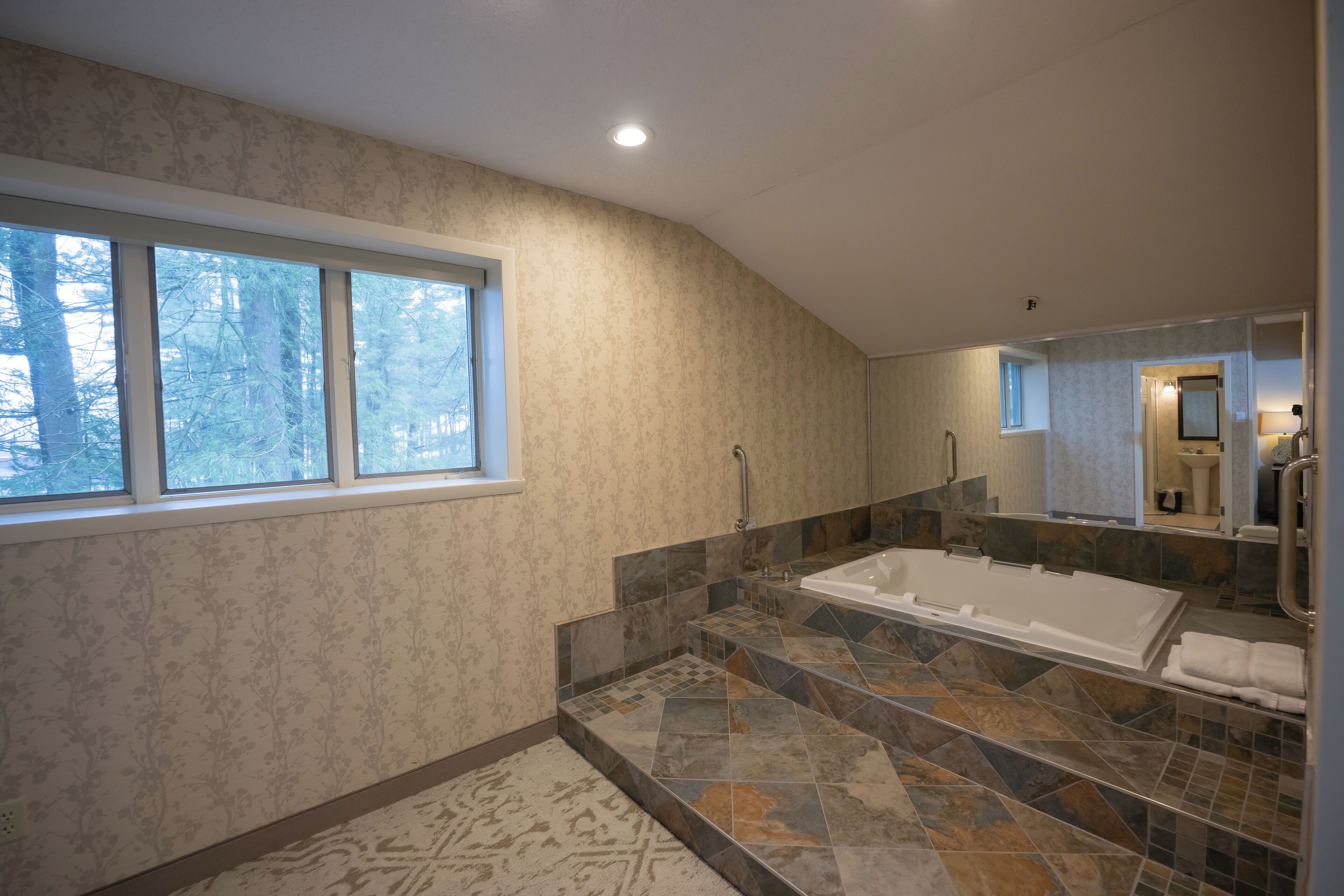 Ein modernes Badezimmer mit einer großen Badewanne, einer begehbaren Dusche und einem Fenster, das für natürliches Licht sorgt.