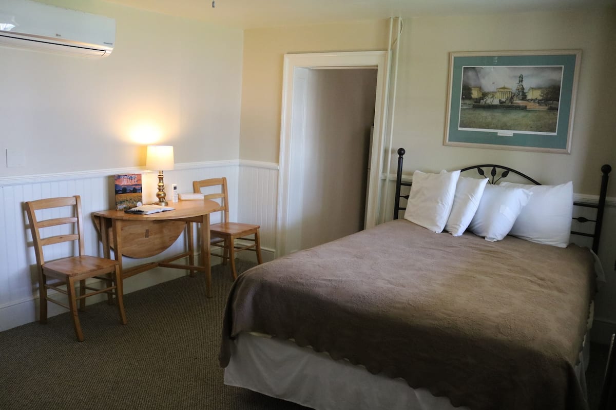 A hotel room with a bed, two chairs, a small table, a lamp, and a framed picture on the wall.