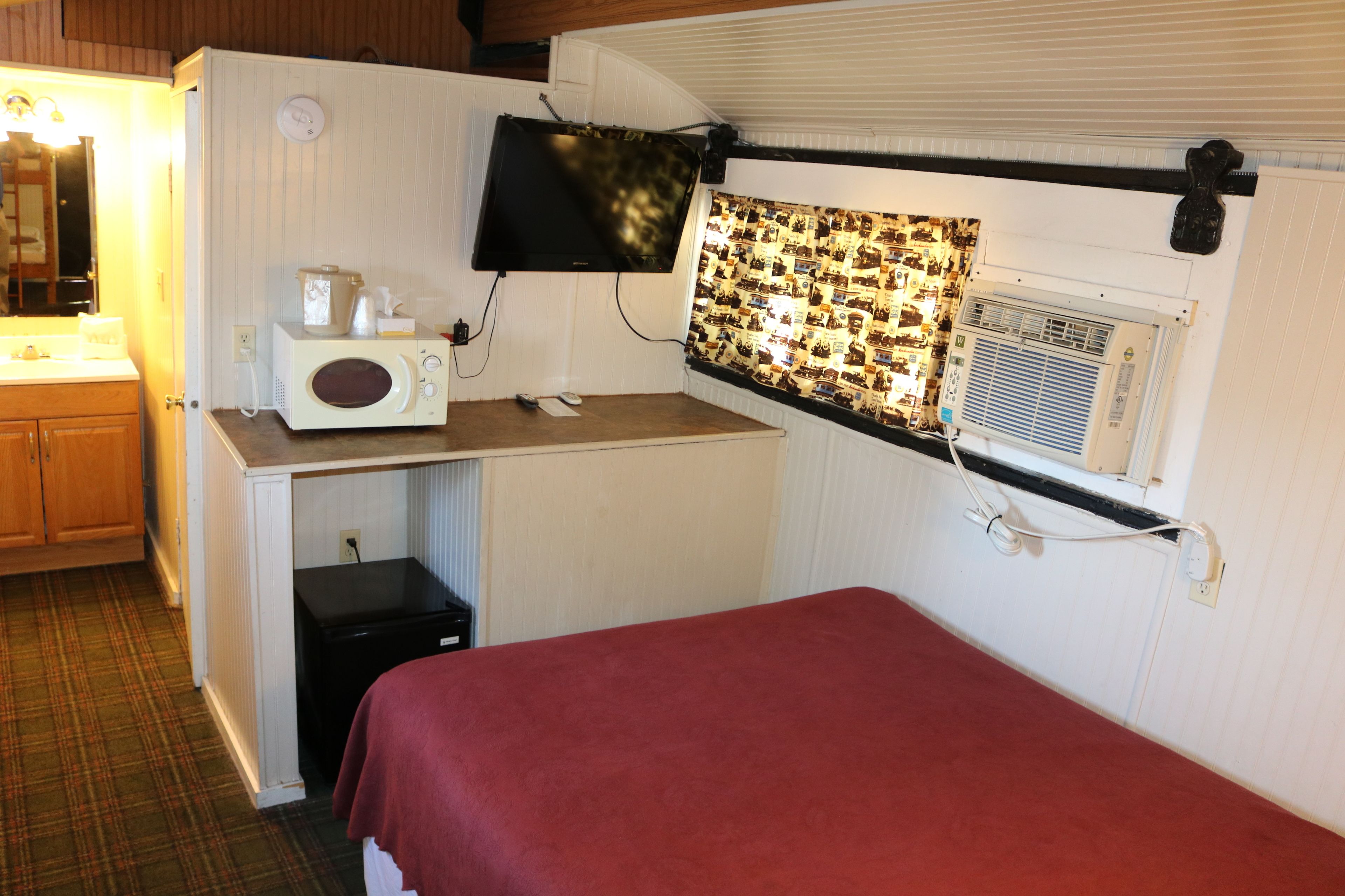 A compact room with a kitchenette, a bed, a television, and a patterned curtain.