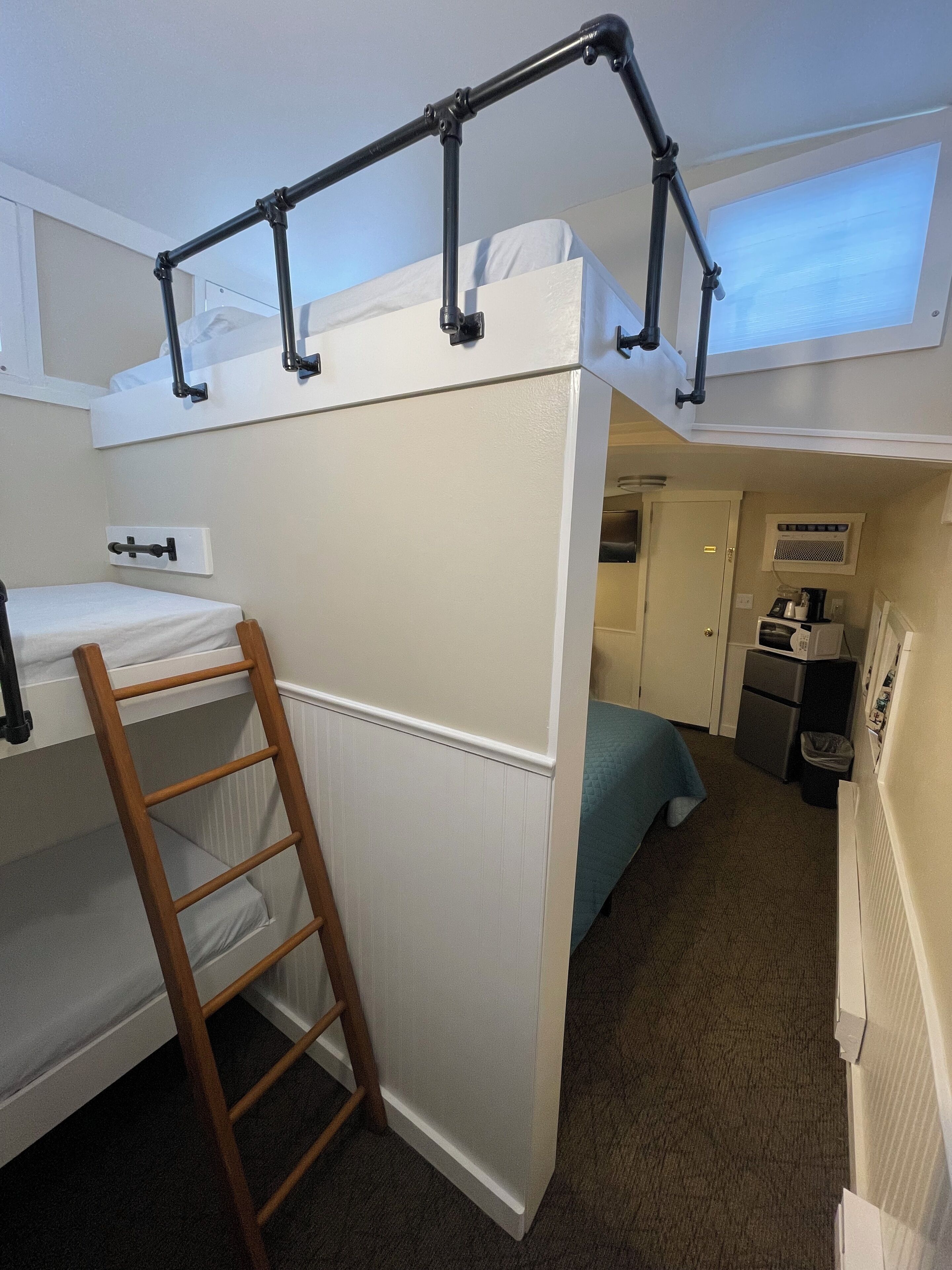 A compact room with bunk beds, a wooden ladder, a kitchenette, and a small bathroom.