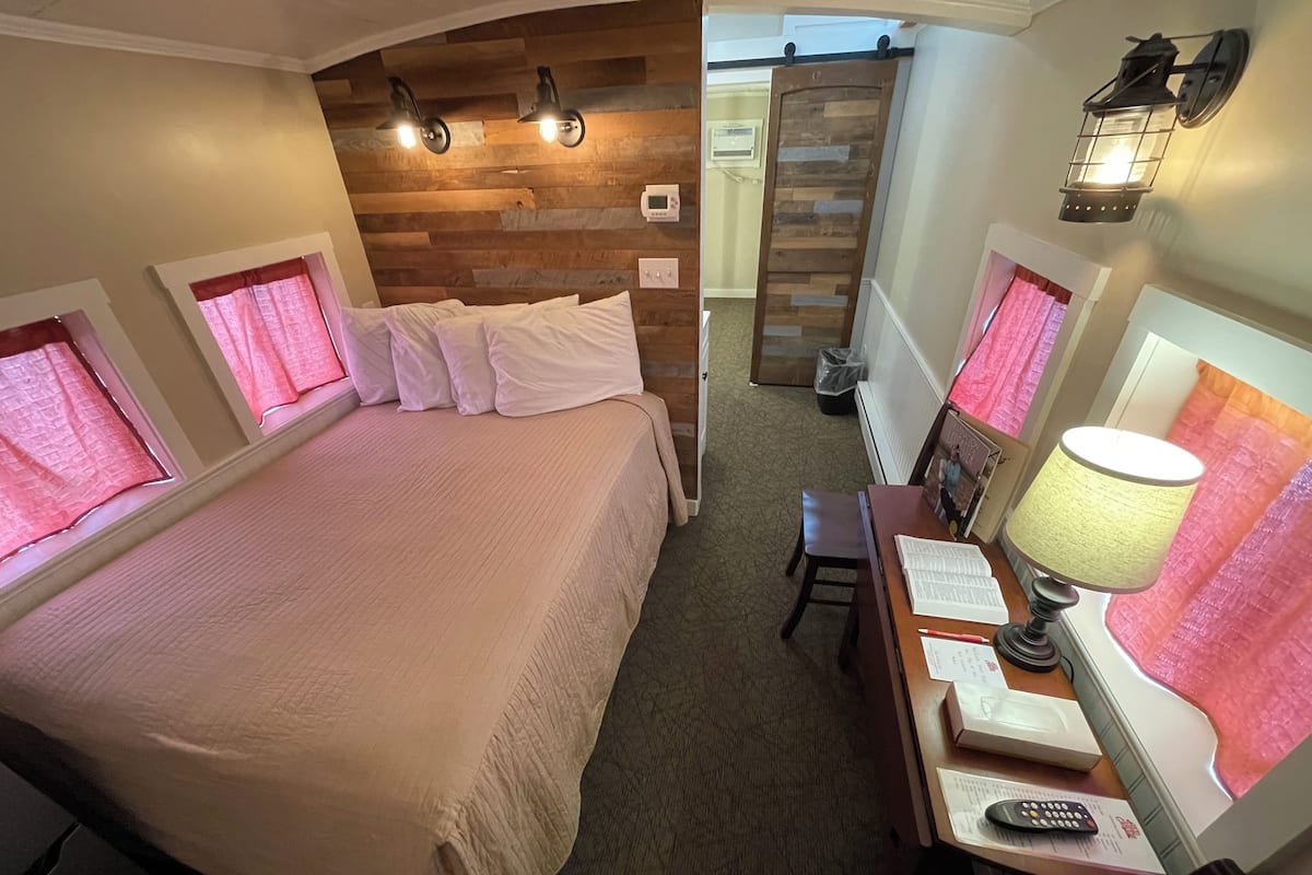 A hotel room with a large bed, a desk with a lamp, and a window with curtains.