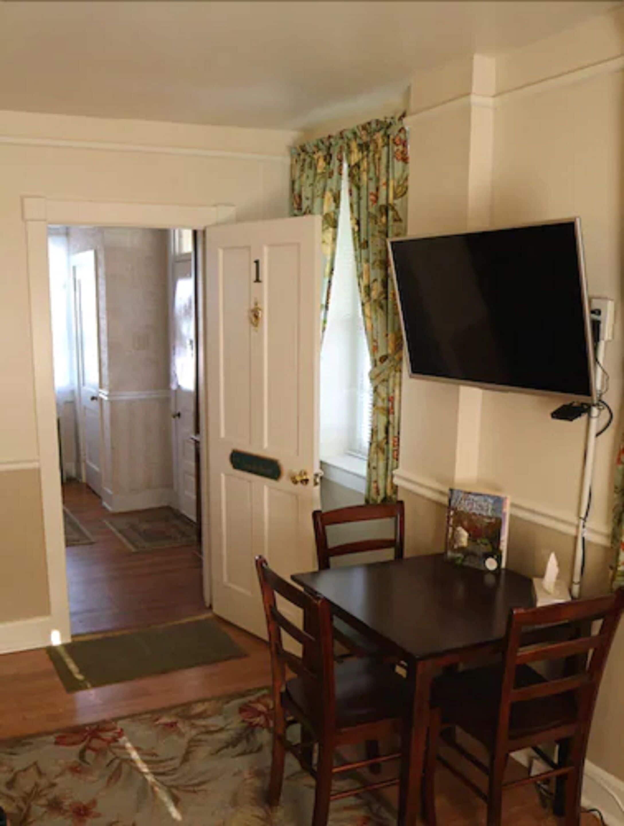 A dining area with a table, chairs, a television mounted on the wall, and a door leading to another room.