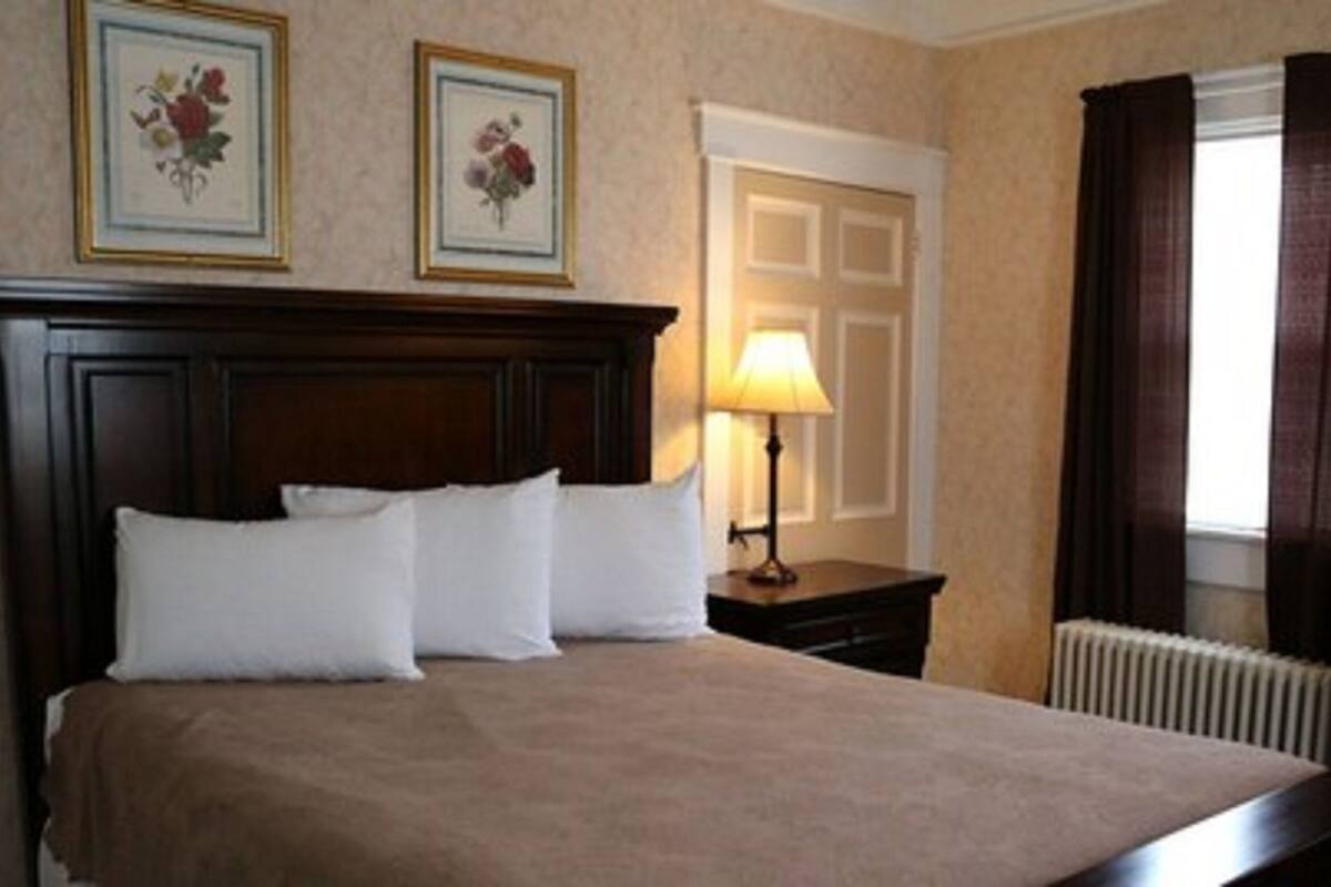 A hotel room with a large bed, a nightstand with a lamp, a radiator, and two framed floral pictures on the wall.
