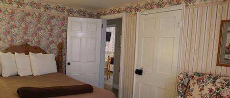 A bedroom with a bed, a chair, and a door leading to another room.