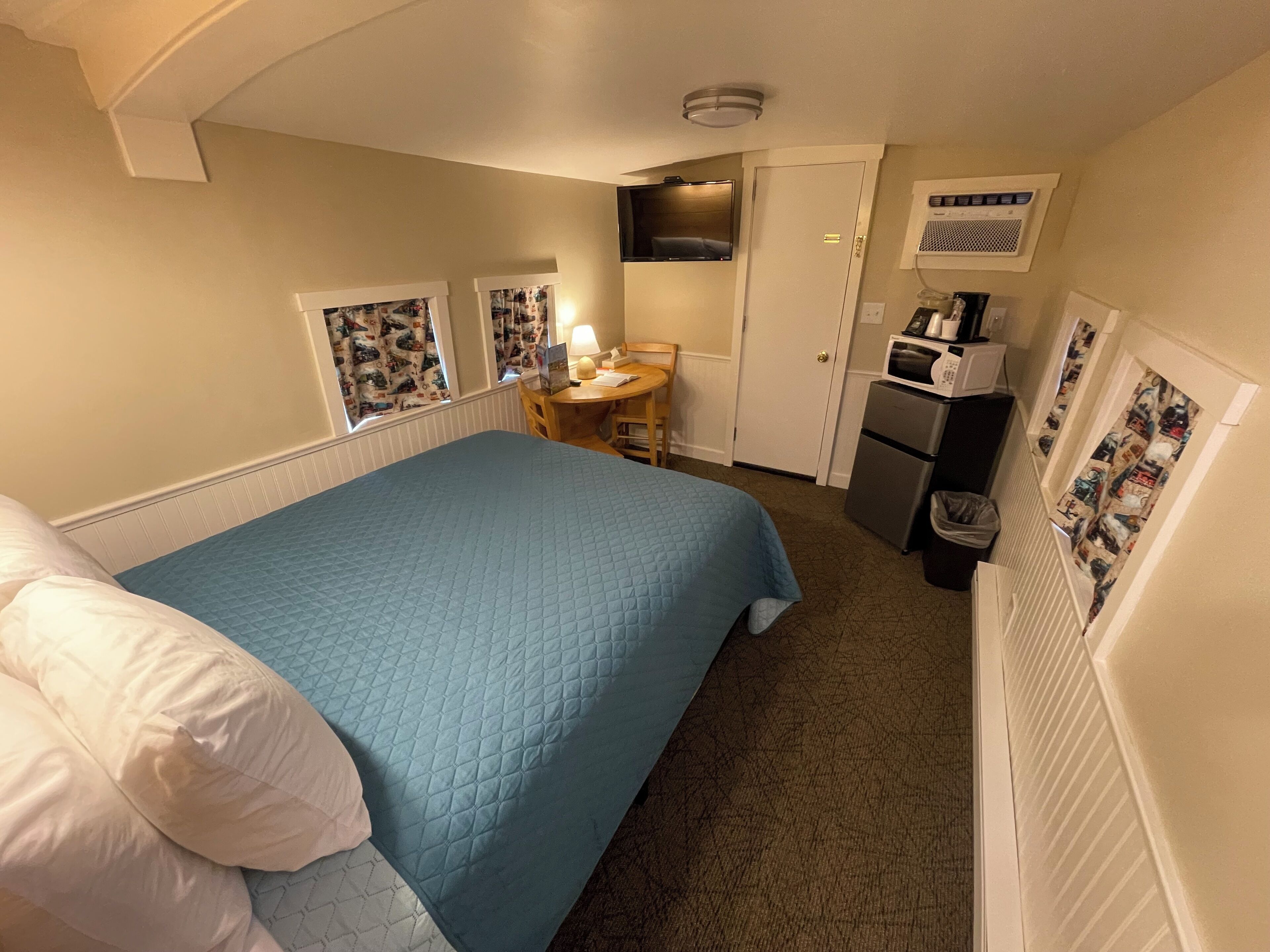 A hotel room with a bed, a desk, a chair, a microwave, and a trash bin.