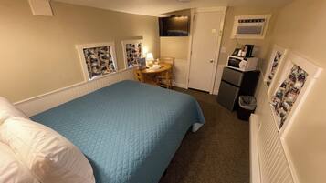 A hotel room with a bed, a desk, a chair, a microwave, and a trash bin.