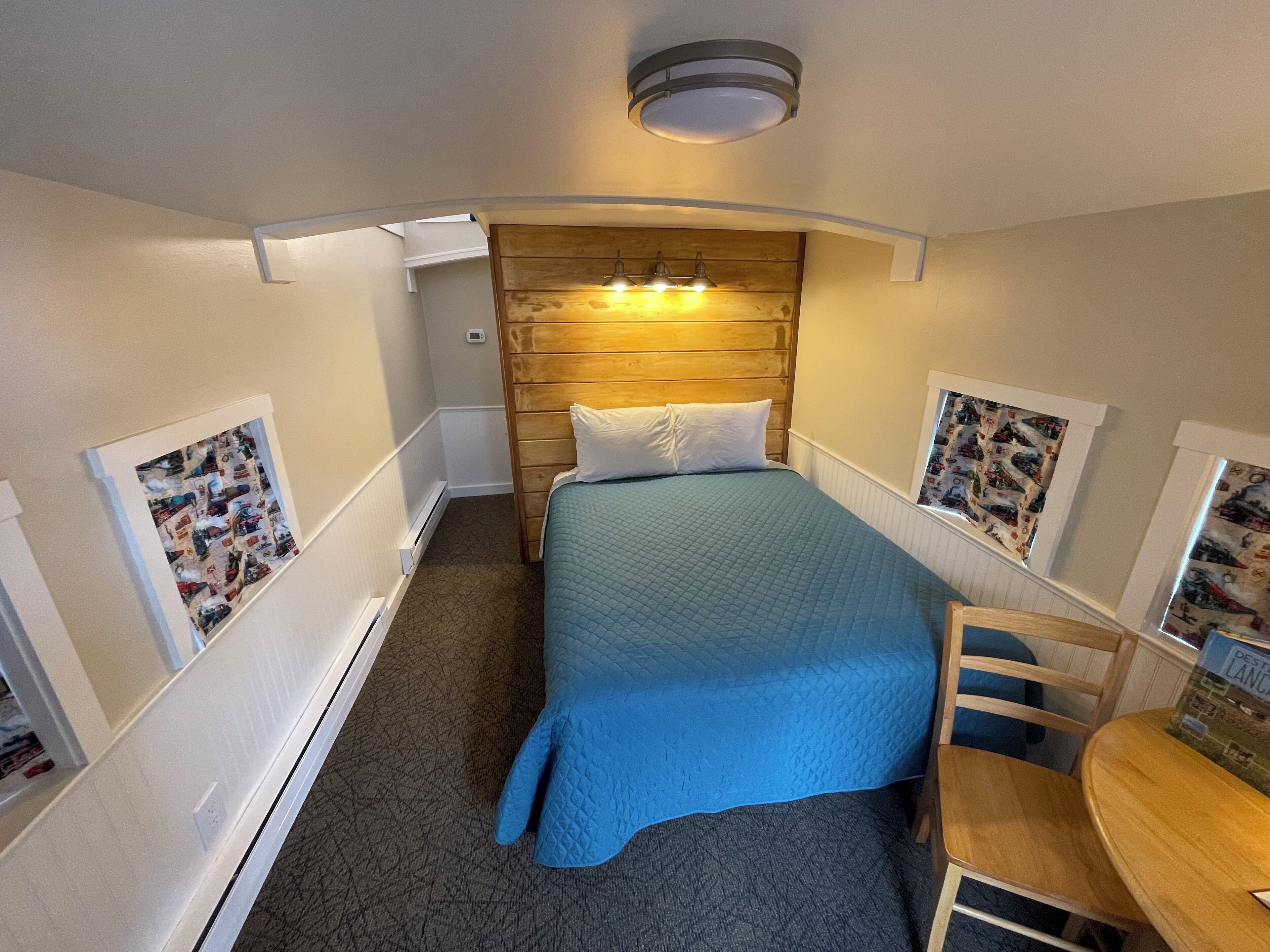 A compact room with a single bed, a wooden headboard, a small table, and two framed pictures on the walls.