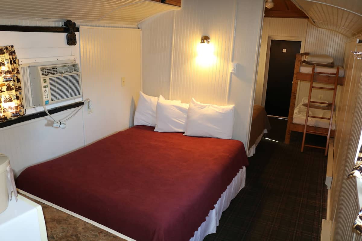 A compact room with a single bed, a small bedside table, a wall-mounted heater, and a ladder for accessing a loft bed.